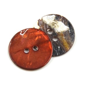 May include: Two round buttons, one is brown with white and black swirls, the other is a shiny orange colour. Both buttons have two holes.