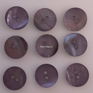 Peut inclure: Neuf boutons ronds de couleur violet foncé disposés en une grille de trois par trois. Chaque bouton présente deux trous centraux pour la fixation et une surface lisse légèrement irisée. Le bouton central porte le texte blanc Mei Match.