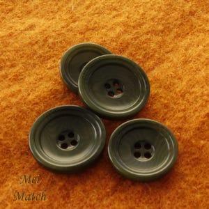 Puede incluir: Cuatro botones de plástico verde oscuro con cuatro agujeros cada uno. Los botones están sobre una superficie naranja peluda.