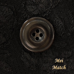 May include: A black button with four holes in the center. The button is on a black fabric background.