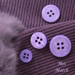 May include: Four purple buttons with four holes each, on a purple knitted fabric background. The buttons have a subtle shimmer.