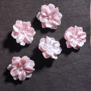 May include: Five individual flower-shaped buttons with a glossy, pearlescent light pink finish. Each button features layered, rounded petals radiating from a central point, creating a dimensional, sculpted appearance with a smooth, reflective surface.