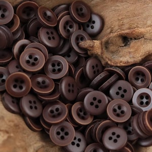 Peut inclure: Une grande collection de boutons ronds marron foncé, chacun doté de quatre trous au centre. Les boutons présentent une finition mate et lisse ainsi qu'un bord extérieur légèrement surélevé, créant une apparence uniforme pour ces attaches.