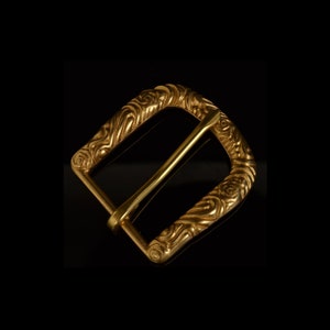 Op de afbeelding: Een gouden metalen gesp met een sierlijk, wervelend ontwerp.