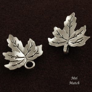 May include: Two silver metal maple leaf charms with a loop for attaching to jewellery or other crafts.