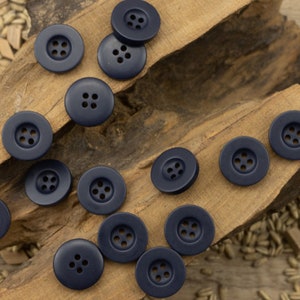 Könnte beinhalten: Eine Sammlung von 14 dunkelblauen Kunststoffknöpfen mit jeweils vier Löchern. Die Knöpfe sind auf einer Holzoberfläche angeordnet.