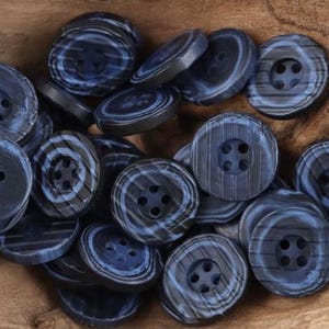 Puede incluir: Una colección de botones con patrones azules y negros, cada uno con cuatro agujeros. Los botones tienen un diseño a rayas y están hechos de un material liso y duro.