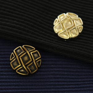 May include: Two gold-toned metal buttons with a geometric design. The buttons have a raised, textured surface and a circular shape.