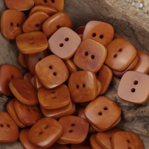 May include: A pile of brown, square-shaped buttons with two holes each. The buttons are made of a wood-like material and have a natural, rustic look.