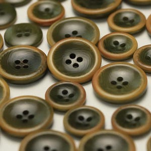 May include: A collection of green and brown buttons with four holes each. The buttons are made of a textured material and have a slightly raised edge.