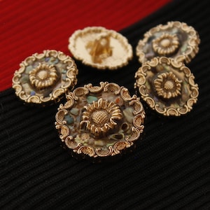 May include: Five gold-toned buttons with a decorative floral design and iridescent shell accents. The buttons are arranged on a black fabric background.