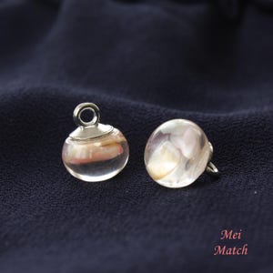 May include: Two clear glass buttons with a silver metal loop on one button. The buttons have a pink and white swirl pattern inside.