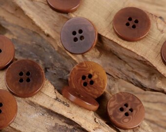 Op de afbeelding: Een verzameling bruine knopen met elk vier gaatjes, in verschillende tinten en patronen. De ronde knopen zijn gemaakt van een glad materiaal en liggen op een houten oppervlak met textuur. Sommige knopen hebben een gemarmerd uiterlijk.