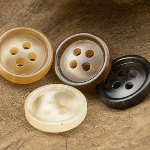 May include: Four buttons with four holes each. Two buttons are brown with a light brown centre, one button is white with a light brown centre, and one button is black.