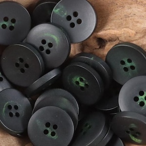 May include: A close-up of a pile of black buttons with green accents. The buttons have four holes each.