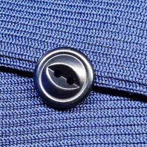 May include: A close-up of a silver button with two holes, sewn onto a blue fabric.