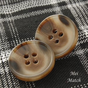 May include: Two brown and white patterned buttons with four holes each. The buttons are on a black and white checked fabric.