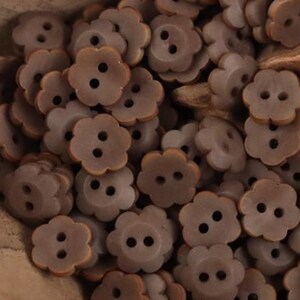 May include: A pile of flower-shaped buttons in various shades of brown. Each button features a scalloped edge and two small holes for sewing. The buttons are grouped together, indicating a large quantity suitable for crafts or sewing.