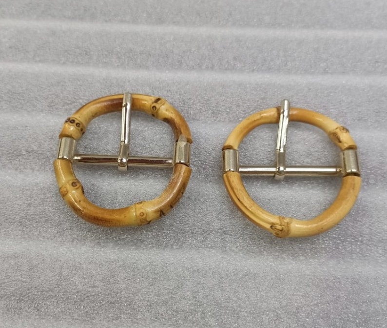May include: Two round, brown bamboo belt buckles with silver metal clasps. The buckles are approximately 2 inches in diameter.