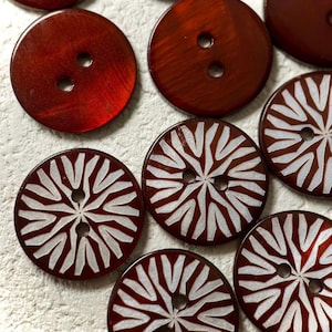 May include: A collection of round, two-hole buttons in a deep reddish-brown color. Some buttons feature a solid, glossy finish, while others display a white, radiating, star-like pattern etched across the surface of the circular button face.