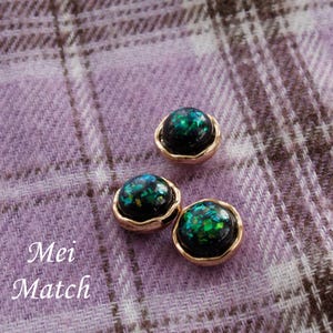 Può includere: Tre orecchini a lobo circolari con base nera e inserti iridescenti verdi e blu, incastonati in una montatura in metallo color oro rosa lucido. Il testo Mei Match è visibile nell'angolo in basso a sinistra dell'immagine.