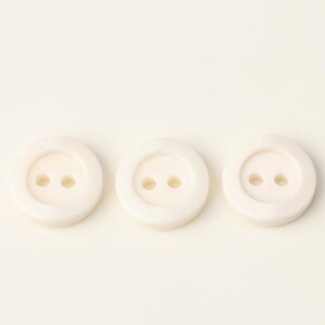 Puede incluir: Tres botones de plástico blanco con dos agujeros cada uno.