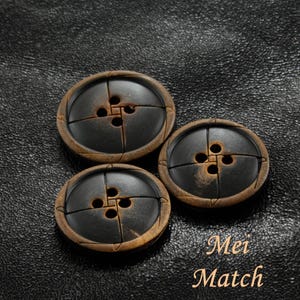 Puede incluir: Tres botones marrones y negros con cuatro agujeros cada uno. Los botones tienen una superficie texturizada y están dispuestos en forma triangular.