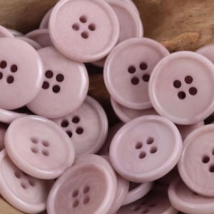 Pode incluir: Um conjunto de botões redondos rosa pálido, cada um com quatro furos. Os botões têm uma aparência ligeiramente marmoreada e estão agrupados. Estes botões são ideais para costura e projetos de artesanato.