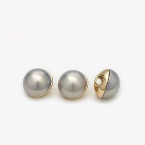 May include: Three round, pearl-like buttons with a gold trim. The buttons are gray and have a slight iridescent sheen.