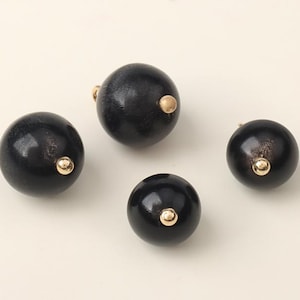 Op de afbeelding: Vier zwarte houten kralen met gouden accenten. De kralen zijn rond en hebben een gladde, gepolijste afwerking.