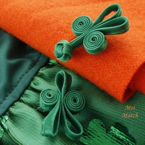 May include: Two green fabric closures with a knotted center, one on a bright orange fabric and the other on a green fabric with a metallic sheen. The text "Mei Match" is visible in the bottom right corner.