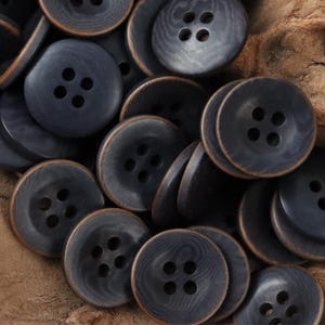 Peut inclure: Une collection de boutons ronds gris foncé avec une texture de grain de bois visible. Chaque bouton présente quatre trous au centre et un bord brun distinct. Les boutons sont disposés en groupe, montrant leur forme circulaire et lisse.
