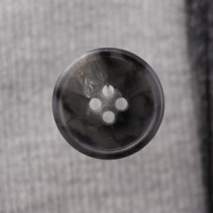 May include: A black and white button with four holes. The button has a marbled pattern.