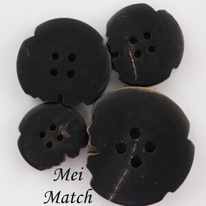 May include: Four black buttons with four holes each. The buttons are made of a natural material with a slightly rough texture. The buttons are different sizes.