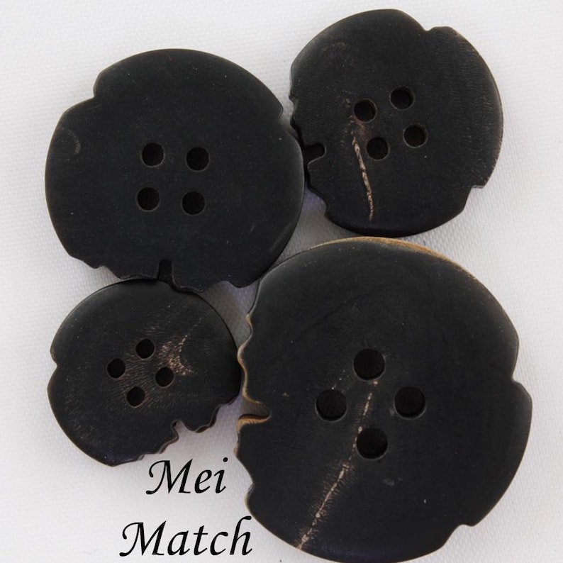 May include: Four black buttons with four holes each. The buttons are made of a natural material with a slightly rough texture. The buttons are different sizes.
