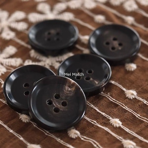 May include: A set of five round, dark brown buttons with a smooth, polished finish. Each button features four central holes for attachment and a slightly recessed center. The text Mei Match is printed in white near the center of the arrangement.