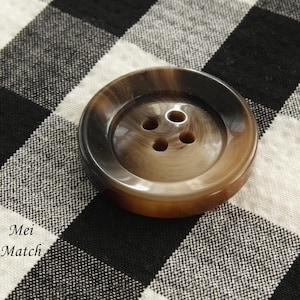 May include: A brown and black button with four holes. The button is made of a smooth, shiny material.