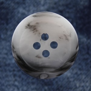 May include: A white button with a marbled pattern and four blue holes.