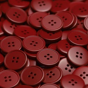 Puede incluir: Una imagen de primer plano de un montón de botones rojos. Los botones son todos del mismo tamaño y forma, y tienen cuatro agujeros cada uno.
