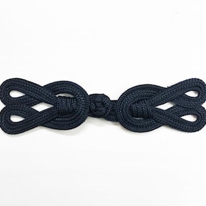 May include: A dark blue fabric button with a knotted design. The button is made of two loops that are connected in the middle.