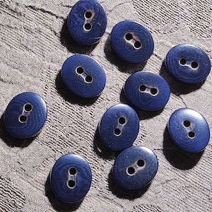 May include: A collection of nine oval-shaped buttons in a deep navy blue color. Each button features a smooth, wood-grain texture and two central holes for attachment, arranged in a scattered pattern across the frame for clear visibility.
