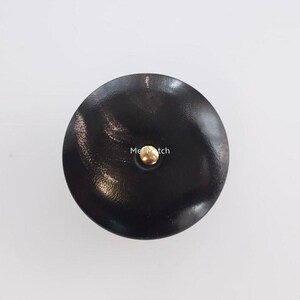 May include: A circular dark brown button with a smooth, slightly reflective surface and a single central gold-toned metal rivet. The text Mei Match is printed in white across the center of the button, positioned just above the gold rivet.