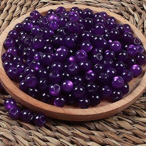 May include: A bowl filled with purple beads. The beads are round and have a glossy finish.