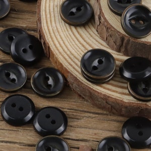 May include: A collection of black plastic buttons with two holes. The buttons are arranged on a wooden surface.