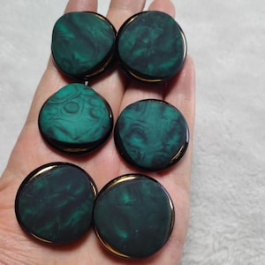 May include: Six dark green and black plugs with a marbled effect. The plugs are round with a gold-colored rim. One plug is a unique teardrop shape. The plugs are shown in a hand.