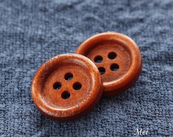 May include: Two brown wooden buttons with four holes each, on a blue fabric background.