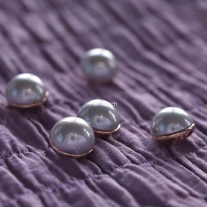 Op de afbeelding: Vier ronde, koepelvormige knopen met een gladde, glanzende lichtgrijze afwerking en een koperkleurige metalen basis. Elke knoop heeft een centraal gat voor bevestiging. Het woord "Mel Fetch" staat in witte tekst tussen de knopen gedrukt.