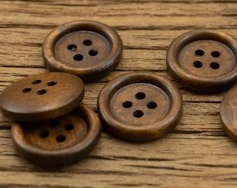 May include: A group of six brown wooden buttons with four holes each. The buttons are arranged in a semi-circle on a wooden surface.