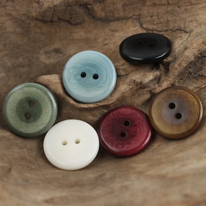 以下が含まれることがあります： 木製の表面に円形に並べられた、異なる色と模様の2穴ボタン6個。ボタンはプラスチック製で、滑らかな仕上がりです。