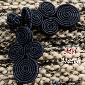 May include: Close-up of navy blue spiral-shaped decorative embellishments. The embellishments are made of a woven material and are arranged in clusters. The background is a textured fabric with black, white, and gray threads. The text "Mei Match" is in the bottom right corner.